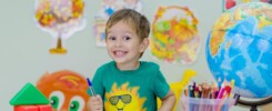 Bambino sorridente seduto alla scrivania con libri e colori. Muro decorato con disegni sullo sfondo