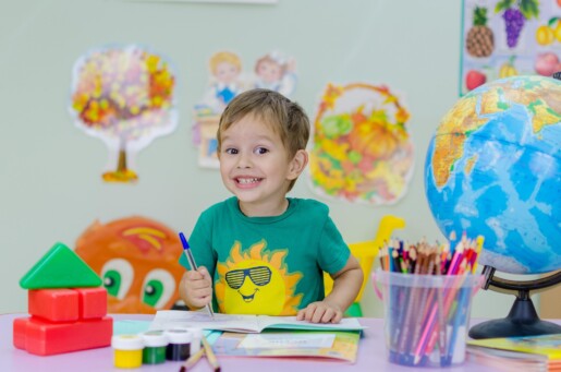 Bambino sorridente seduto alla scrivania con libri e colori. Muro decorato con disegni sullo sfondo