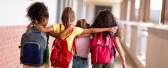 Quattro bambine camminano di spalle abbracciate tra i corridoi scolastici